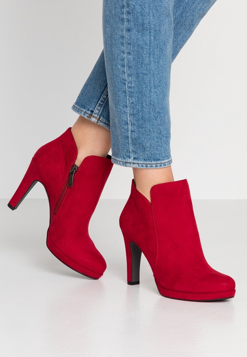 Bottines en daim rouge à talon haut, dotées d'une fermeture éclair sur le côté et d'un design élégant et moderne. Texture lisse et couleur audacieuse.