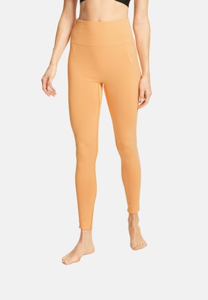 Leggings de couleur pêche avec une taille haute, fabriqués à partir d'un matériau extensible. Présentent une texture lisse et un branding minimal sur le côté.