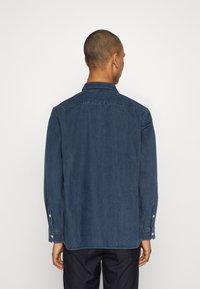Denim shirt met een puntige kraag, lange mouwen en knoopmanchetten. Heeft een effen donkerblauwe kleur met een gladde, lichtjes textuur. 
