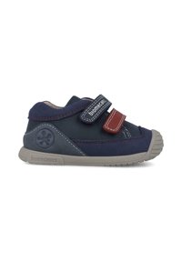 Chaussures en suède bleu marine avec des semelles en caoutchouc gris, deux bandes velcro rouges et bleu marine, et des détails en coutures blanches. Pointe arrondie et logo au talon.