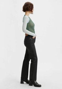 Zelený síťovaný top bez rukávů překrytý světle modrou dlouhou košilí, v kombinaci s černými džíny s vysokým pasem a masivními černými podpatky.