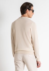 Maglione beige lavorato a maglia con scollatura rotonda, vestibilità slim e orli a coste, abbinato a pantaloni di colore chiaro. Texture liscia.