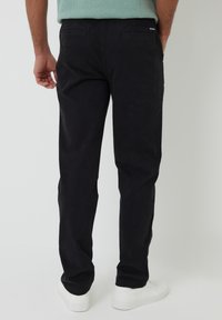 Pantalones de algodón negros con diseño de pierna recta. Presentan dos bolsillos traseros y un pequeño logo. Llevados con zapatillas blancas.