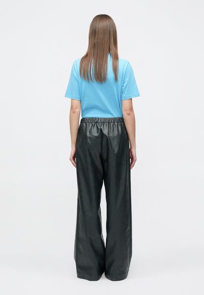 Μπλε κοντομάνικη μπλούζα σε συνδυασμό με μαύρο δερμάτινο παντελόνι φαρδιάς γραμμής με ελαστική μέση, σε άποψη από πίσω.