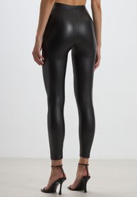 Leggings neri a vita alta in un materiale lucido e liscio, aderenti dalla vita alla caviglia. Abbinati a tacchi alti neri con cinturini.