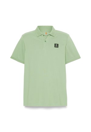Koszulka polo w jasnym zielonym kolorze, wykonana z teksturowanej tkaniny, z kołnierzykiem i zapięciem na trzy guziki. Posiada czarne logo w kształcie kwadratu na lewej piersi.