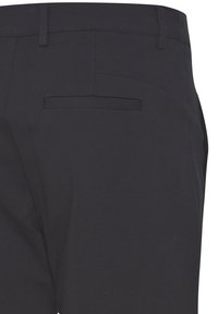 Gros plan sur un pantalon noir montrant la ceinture, les passants de ceinture et une poche passepoilée arrière côté droit.