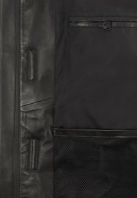 Sort jakke med sektioner i læder og stof, med en stor netlomme og en knaplukket brystlomme. Glat tekstur og strømlinet design.