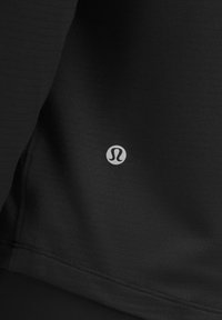 Crni atletski top s teksturiranom tkaninom, s suptilnim logotipom sa strane i čistim, prilagođenim dizajnom.