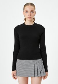 Czarny prążkowany sweter z długimi rękawami i okrągłym dekoltem, zestawiony z czarno-białą spódnicą w kratę w stylu houndstooth z plisami.
