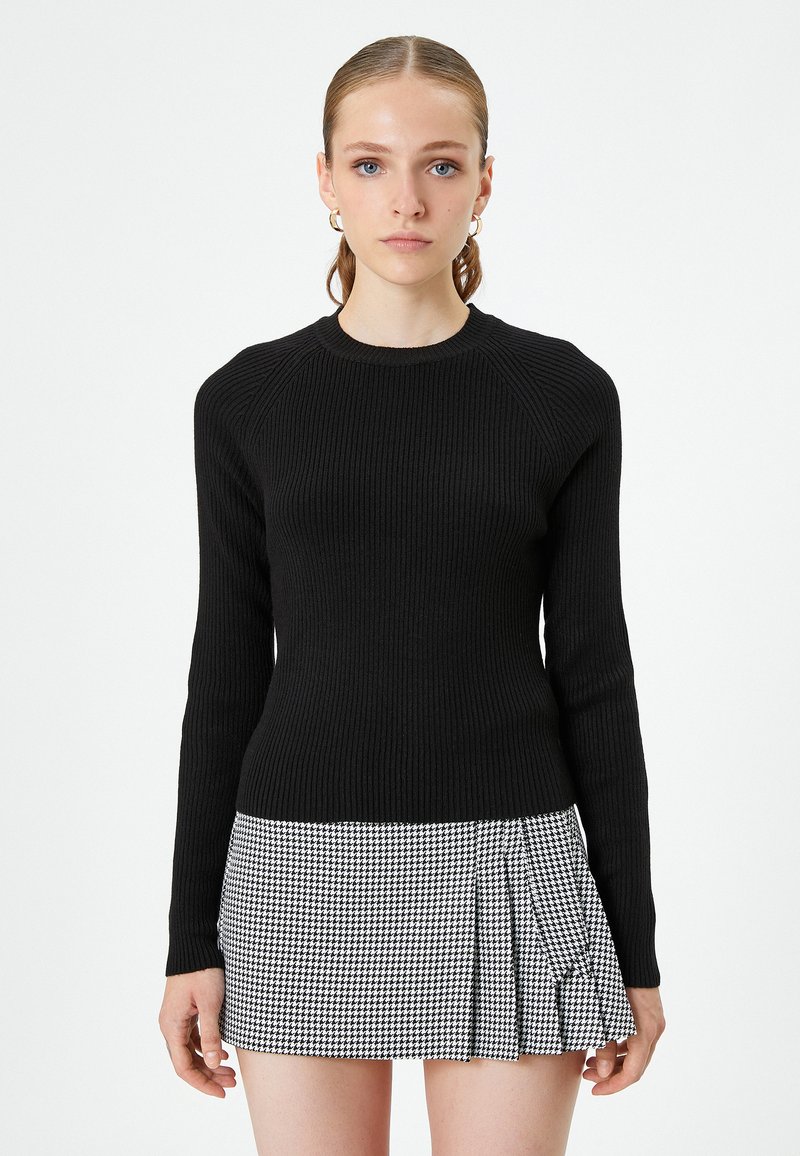 Czarny prążkowany sweter z długimi rękawami i okrągłym dekoltem, zestawiony z czarno-białą spódnicą w kratę w stylu houndstooth z plisami.