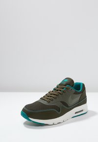 Nike Air Max Sneaker in Olivgrün mit türkisfarbenen Akzenten. Obermaterial aus Mesh und Synthetik, weiße Zwischensohle, runde Zehenpartie und strukturierte Sohle.