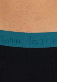 Boxer da uomo neri con un elastico blu in vita che presenta testo in rilievo. Il tessuto sembra liscio e aderente, mettendo in risalto una vista ravvicinata.