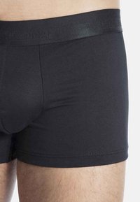 Černé boxerky vyrobené z hladkého materiálu s elastickým pasem, mají těsný střih a jednoduchý design bez vzorů nebo akcentů.