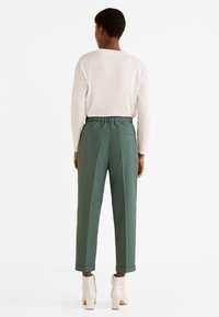 Groene, hoog-gerende broeken met een relaxte pasvorm, gemaakt van een textuurstof en met een elastische tailleband. Gecombineerd met een witte blouse met lange mouwen.