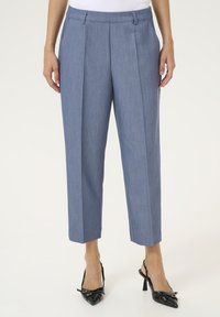 Pantaloni su misura azzurro chiaro con pieghe frontali, lunghezza alla caviglia e una texture liscia. Indossati con scarpe nere con tacco e punte appuntite.