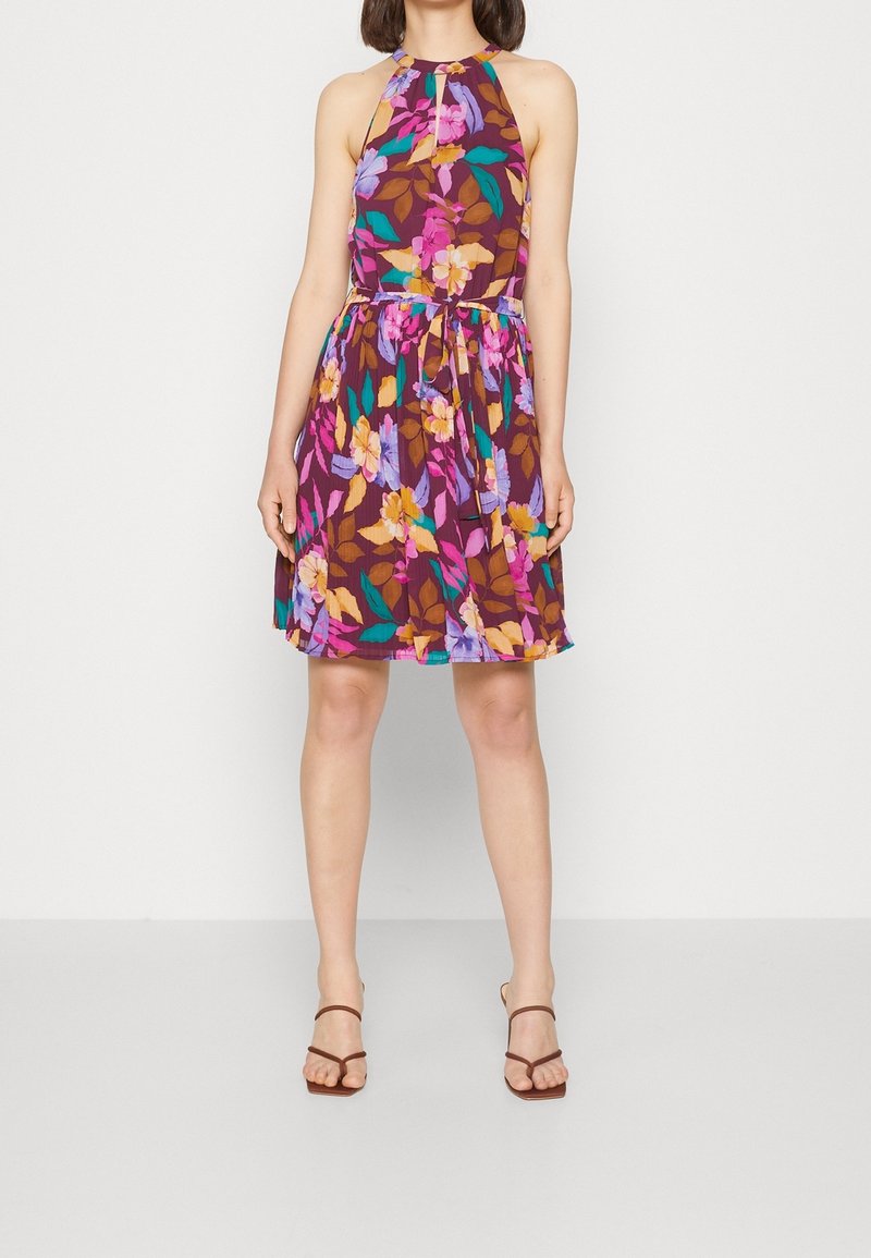 Femme portant une robe sans manches à col licou avec un motif floral multicolore et des sandales fines marron à brides.