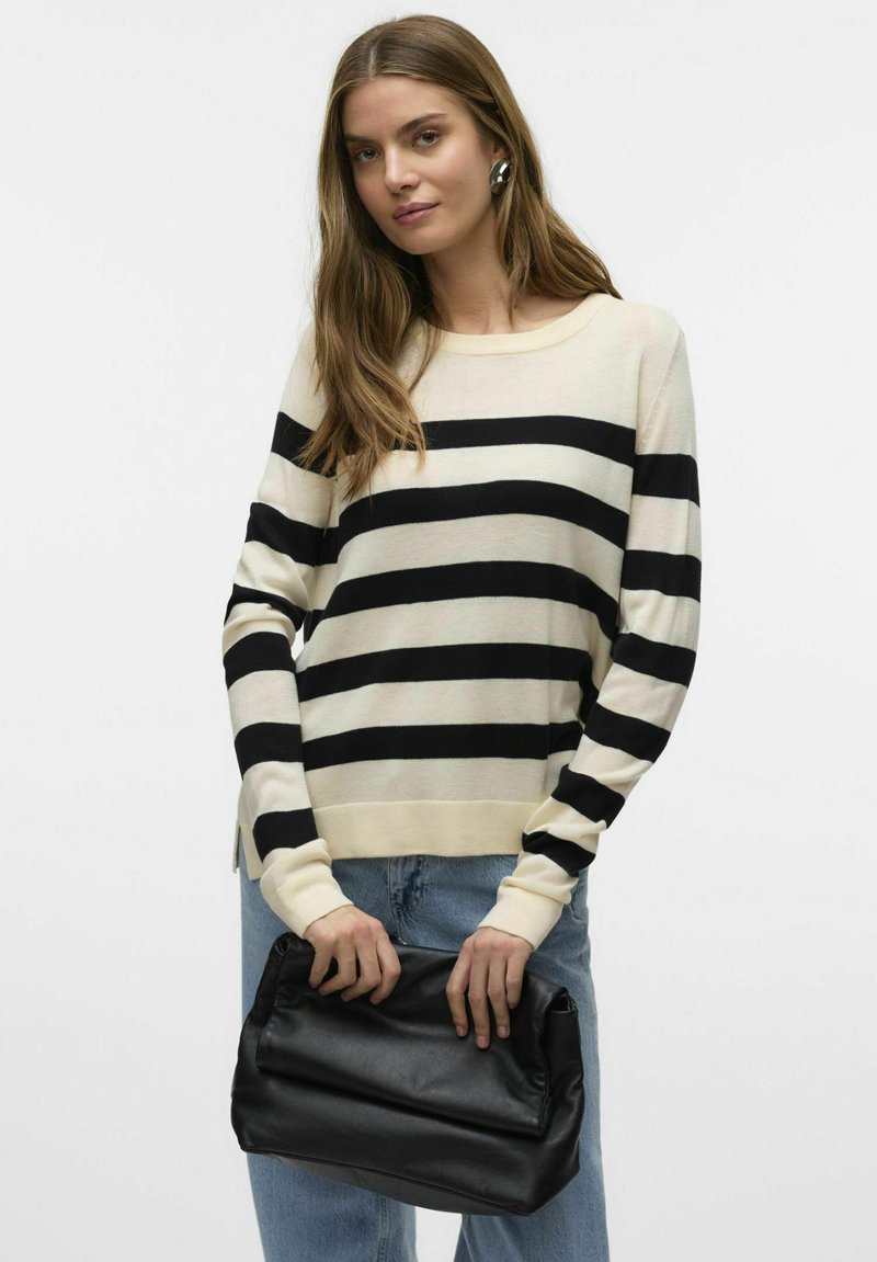 Maglione a righe in crema e nero, realizzato in materiale leggero. Presenta maniche lunghe, polsini a coste e una vestibilità rilassata. Tiene una borsa nera.