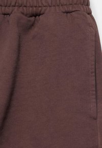 Taille élastique et poche latérale sur pantalon ou short en tissu doux marron.