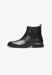 Botas Chelsea de cuero negro con laterales elásticos, punta redonda y tirador; presentan una textura suave y un tacón bajo.