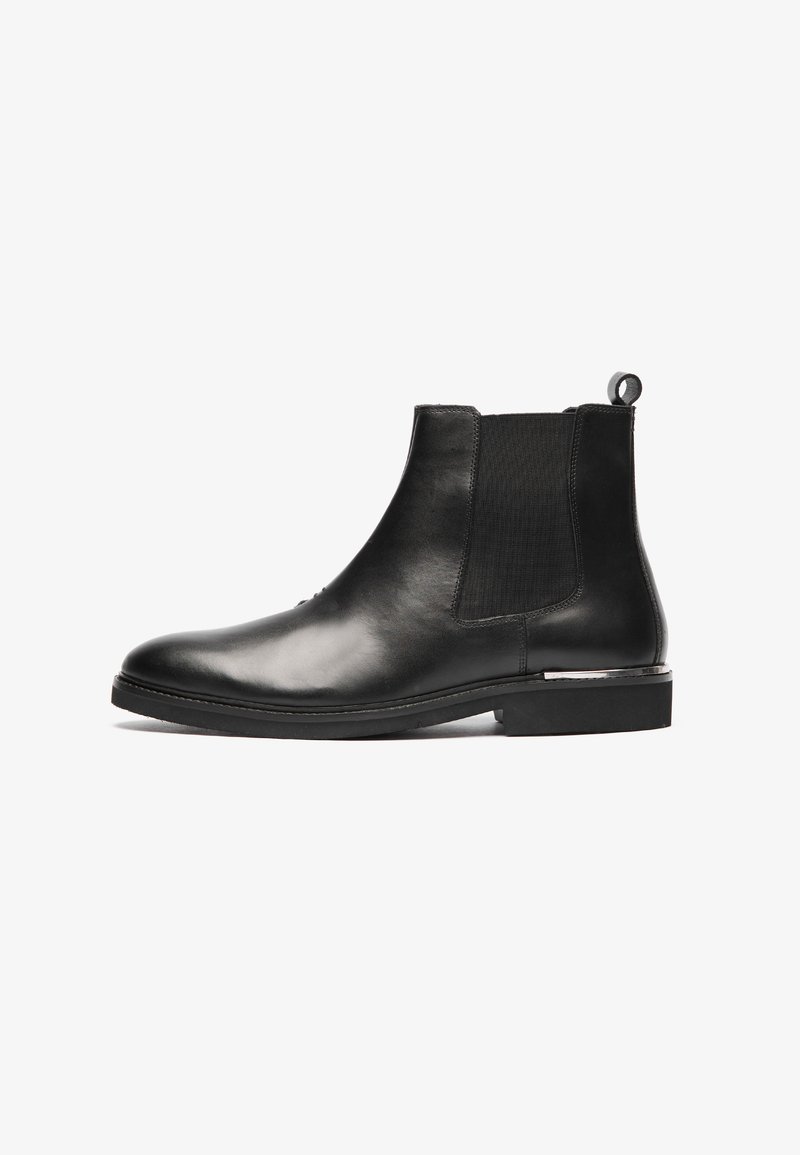Botas Chelsea de cuero negro con laterales elásticos, punta redonda y tirador; presentan una textura suave y un tacón bajo.