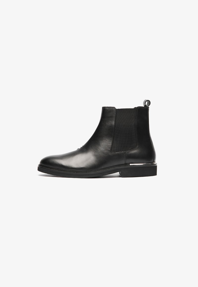 Bottines Chelsea en cuir noir avec des côtés élastiques, bout rond et une languette; présentent une texture lisse et un talon bas.