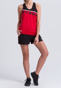 Top deportivo atlético rojo y negro con rayas blancas y acentos negros, combinado con pantalones cortos negros y zapatillas deportivas negras.