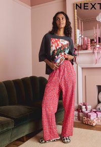 Red checked pajama pants with a loose fit, paired with a dark graphic t-shirt featuring colorful holiday designs. Black and white slippers.