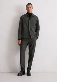 Szara marynarka w prążki z kołnierzem i kieszenią, zestawiona z dopasowanymi zwężanymi spodniami. Całość uzupełniają czarne skórzane buty.