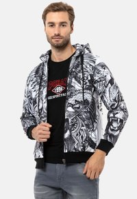 Hooded-Jacke mit einem schwarz-weißen grafischen Design eines Löwen und komplizierten Mustern, aus leichtem Stoff mit gerippten Bündchen.