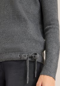 Grijze geribde trui met een trekkoord aan de onderkant en zilveren accenten, gemaakt van zacht materiaal en met een textuurlijke uitstraling.