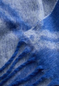 Blå og lyseblå uld tørklæde med en blød tekstur, der har frynseender og et subtilt gradientmønster gennemgående.