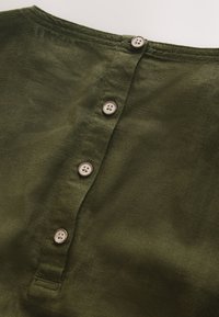 Section de chemise en lin vert olive avec quatre boutons beiges attachés le long de la patte de boutonnage avant.