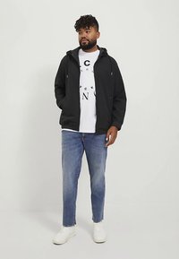 Black hooded jacket with a smooth texture, worn over a white graphic t-shirt, paired with light blue jeans and white sneakers.