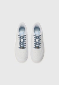 Des chaussures de sport blanches avec des détails perforés, des lacets à motif bleu foncé et blanc, et des semelles intérieures bleu clair. Elles présentent un logo distinct sur le côté.