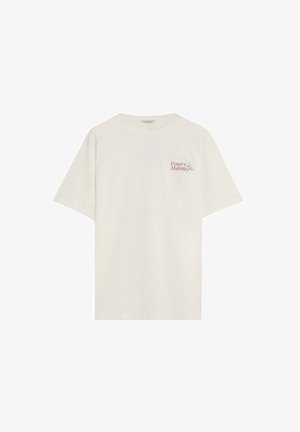 Camiseta crema de manga corta con texto "Fabricación de cerámica" y un pequeño gráfico de un torno de alfarero en el área del pecho izquierdo.