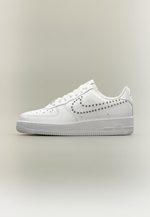 Λευκό χαμηλό sneaker με διάτρητο σχέδιο Nike swoosh στο πλάι, λευκά κορδόνια και υφασμένο πέλμα σε ουδέτερο φόντο.