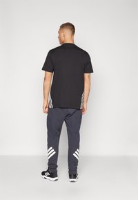 Black t-shirt with short sleeves, paired with dark gray sweatpants featuring white stripe accents on the sides and ankles. Black athletic shoes.