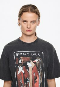 Camiseta negra de gran tamaño con un diseño gráfico floral colorido. El escote es redondo y la tela parece suave y desgastada.