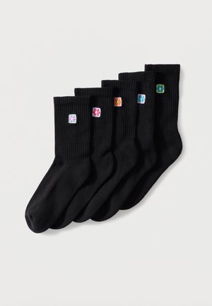 Six chaussettes noires côtelées avec différentes petites fleurs colorées brodées près du haut, disposées en ligne sur un fond blanc.