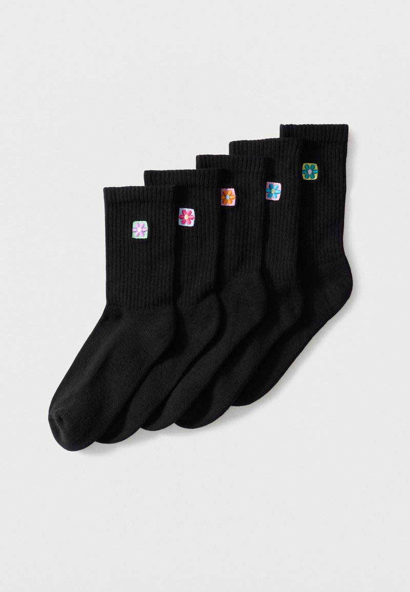 Six chaussettes noires côtelées avec différentes petites fleurs colorées brodées près du haut, disposées en ligne sur un fond blanc.