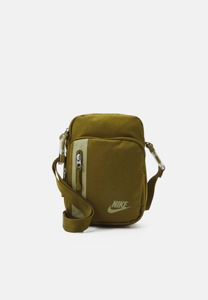 Petit sac d'épaule Nike vert olive avec poche zippée à l'avant, sangle ajustable et logo en bas à droite sur fond blanc.