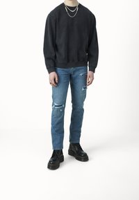 Černá mikina, modré roztrhané džíny s dírami, černé šněrovací boty, vrstvené stříbrné náhrdelníky a prsten na levé ruce.