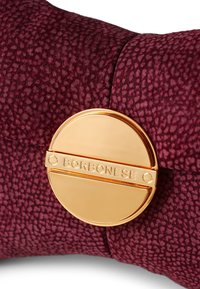 Bordeauxfarbenes strukturiertes Material mit einem goldenen runden Verschluss, der den eingravierten Namen "BORBONESE" trägt. Nahaufnahme, die die Beschläge und die Textur betont.