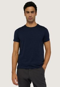 Námořnická modrá bavlněná trička s kulatým výstřihem a krátkými rukávy, s malým logem na levé straně hrudi. Hladká textura, klasický střih.