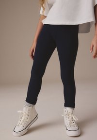 Tumesinised retuusid, mis on valmistatud venivast materjalist, tihedalt istuva lõikega, kombineeritud valgete kõrgete tenniste ja hallide sokkidega.