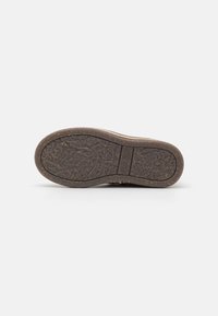 Semelle de chaussure en caoutchouc brun avec un motif texturé, bords légèrement incurvés et empreinte de logo visible, présentant une finition naturelle et rugueuse.