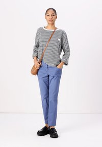 Maglietta a righe a maniche lunghe con scollo rotondo, abbinata a pantaloni azzurri chiari e scarpe con il plateau nere. Piccola borsa a tracolla marrone.
