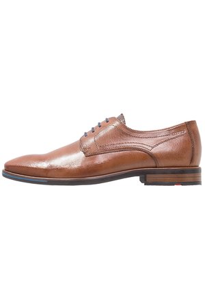 Braune Lederhalbschuhe mit glatter Oberfläche, spitzer Zehenform, blauen Schnürsenkeln und einem gestapelten Holzabsatz, der an der Basis einen roten Akzent hat.