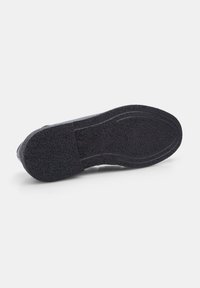 Suela de zapato de goma negra con acabado texturizado, forma redondeada y ligero arco. Presenta ranuras para tracción y durabilidad.
